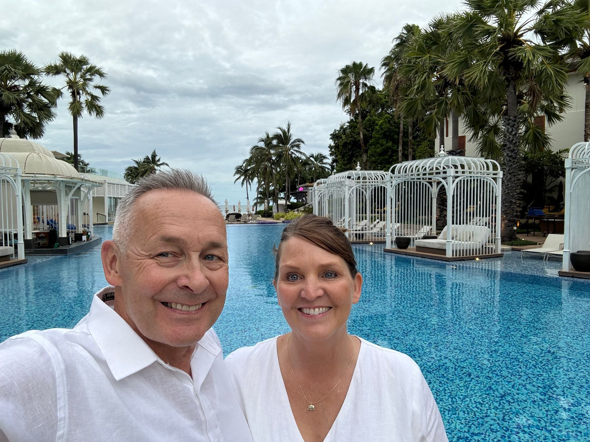 Tyke and Tina smiling together at a tropical resort pool — living their early retirement adventure.